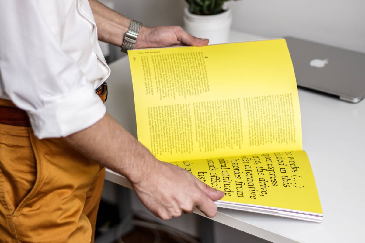 Man flips through magazine with yellow pages and black text