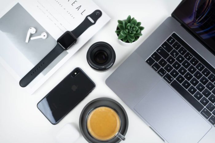 Aerial photo of laptop, smartphone, AppleWatch, Airpods, coffee, and a plant sitting on top of desk
