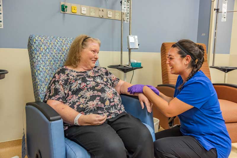 Female nurse in blue scrubs laughs with female patient