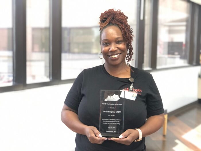 Jovin UofL Pharmacy Services Team Member Jovin Hughes holds an award while smiling